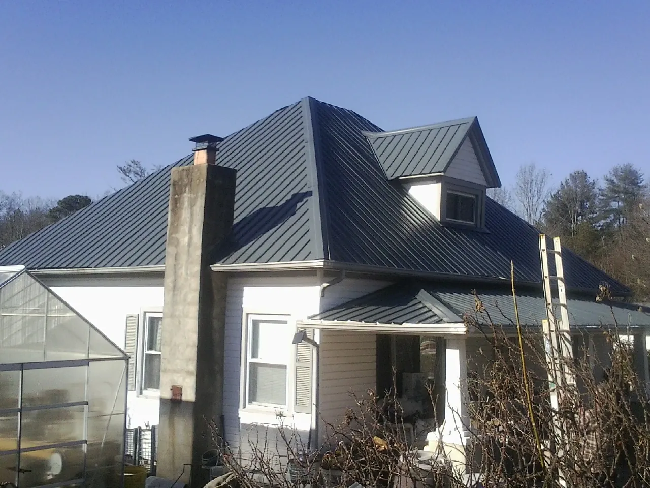 Dark blue standing seam metal roof on a white farmhouse with dormer — Slate & Tile Roof Repair by Roofing Brothers in Seabrook